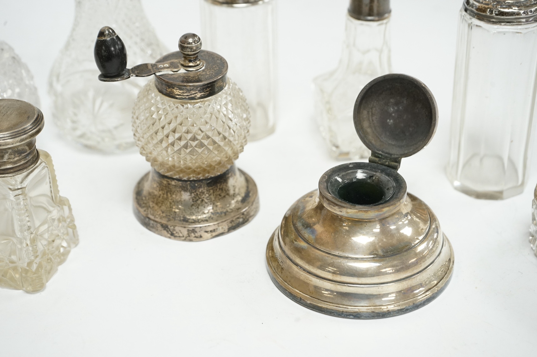A late Victorian silver mounted cut glass pepper grinder, John Grinsell & Sons, Birmingham, 1886, 89mm, a silver mounted inkwell and seven assorted silver mounted glass toilet jars. Condition - poor to fair